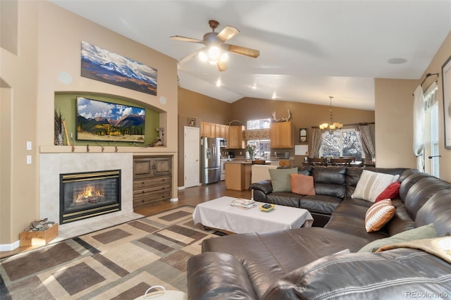 living room with a tile fireplace, light hardwood / wood-style flooring, ceiling fan with notable chandelier, and lofted ceiling