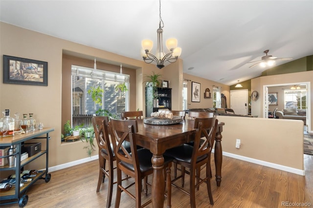 dining space with wood-type flooring, ceiling fan with notable chandelier, a wealth of natural light, and lofted ceiling