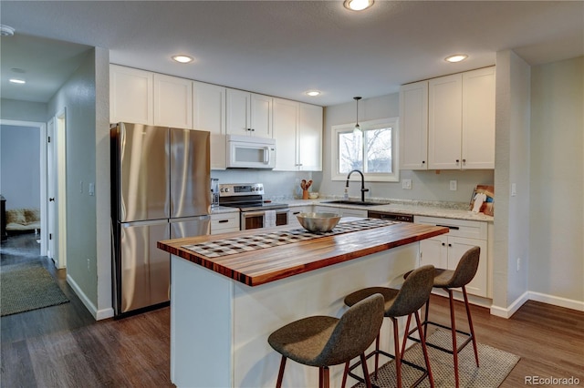 kitchen with white cabinets, butcher block countertops, dark wood-type flooring, stainless steel appliances, and a sink