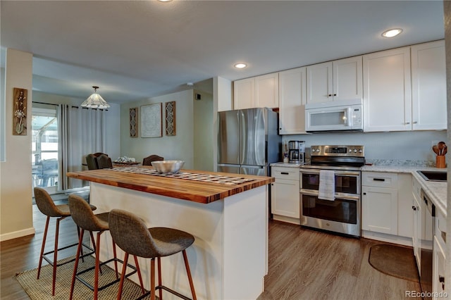 kitchen with white cabinets, wooden counters, appliances with stainless steel finishes, a center island, and dark wood-style floors