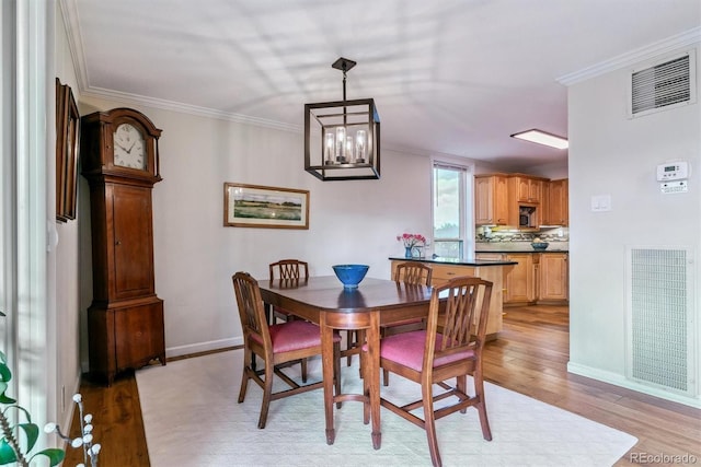 dining room with light wood finished floors, visible vents, and ornamental molding