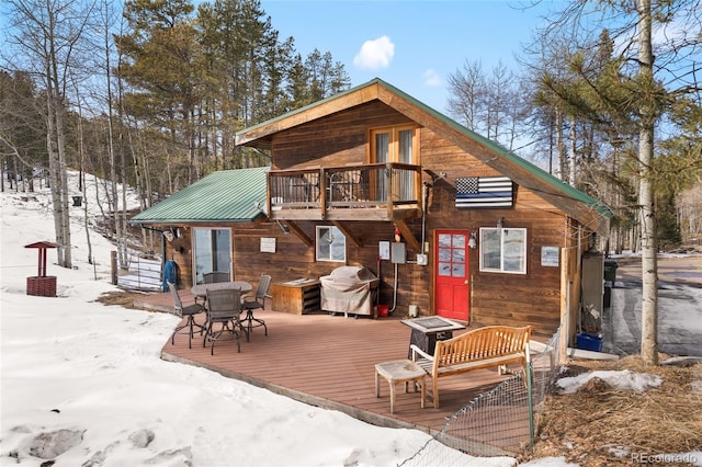 snow covered property with a deck, metal roof, and a balcony