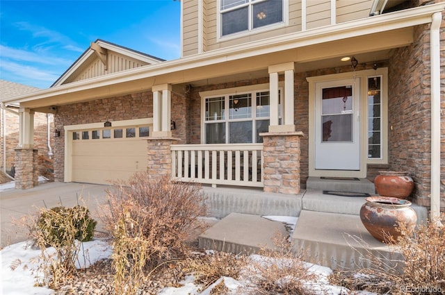 snow covered property entrance featuring a porch, concrete driveway, an attached garage, board and batten siding, and stone siding