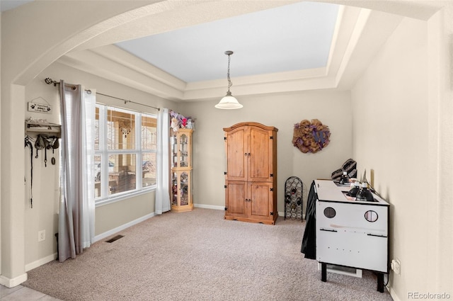 interior space with arched walkways, a raised ceiling, light carpet, and baseboards