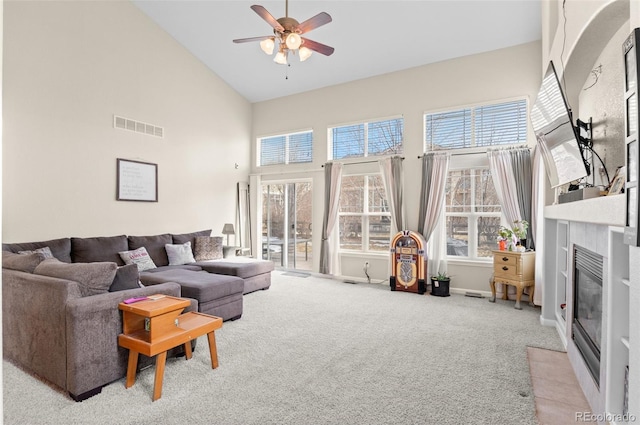 living area featuring visible vents, a ceiling fan, light colored carpet, a glass covered fireplace, and high vaulted ceiling