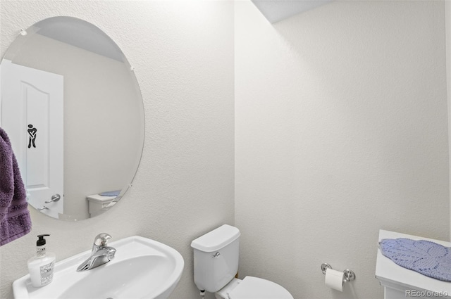 bathroom with toilet, a sink, and a textured wall