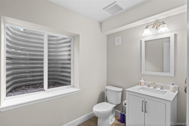 bathroom with toilet, vanity, visible vents, and baseboards