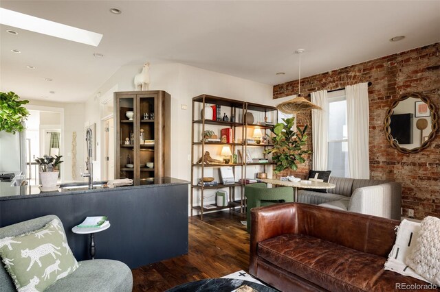 living room featuring dark hardwood / wood-style floors, brick wall, and a skylight