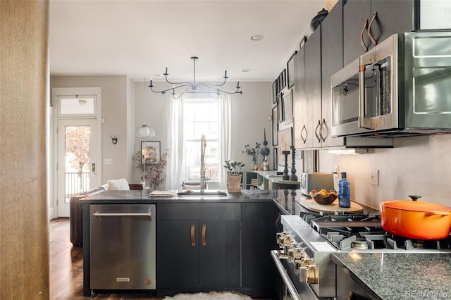 kitchen featuring dark hardwood / wood-style flooring, stainless steel appliances, sink, dark stone countertops, and hanging light fixtures