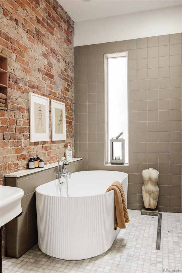 bathroom with a tub to relax in, tile walls, and brick wall