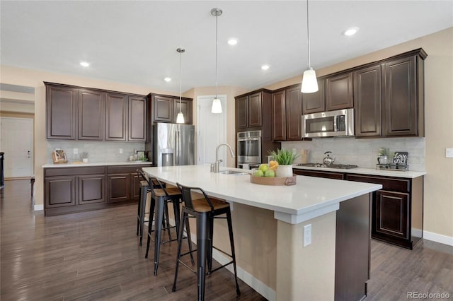 kitchen with a breakfast bar, dark wood finished floors, a kitchen island with sink, stainless steel appliances, and dark brown cabinets