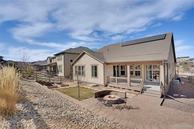 rear view of house featuring a fire pit, roof mounted solar panels, a patio, roof with shingles, and covered porch