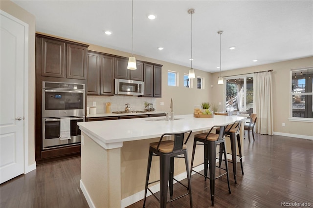 kitchen with stainless steel appliances, light countertops, tasteful backsplash, dark wood-type flooring, and dark brown cabinets
