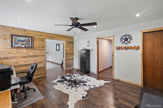 home office featuring ceiling fan, a textured ceiling, wooden walls, and dark hardwood / wood-style floors