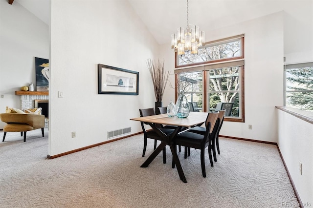 dining area featuring light carpet, a fireplace, high vaulted ceiling, and a chandelier