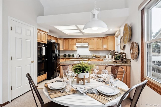 kitchen featuring sink, light stone counters, kitchen peninsula, decorative light fixtures, and black appliances