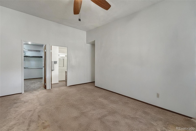 unfurnished bedroom with ensuite bath, ceiling fan, a textured ceiling, light carpet, and a walk in closet