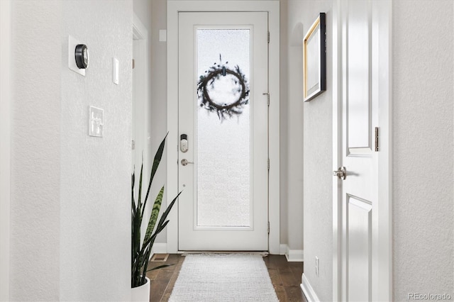 doorway to outside featuring dark wood-style floors, a textured wall, and baseboards