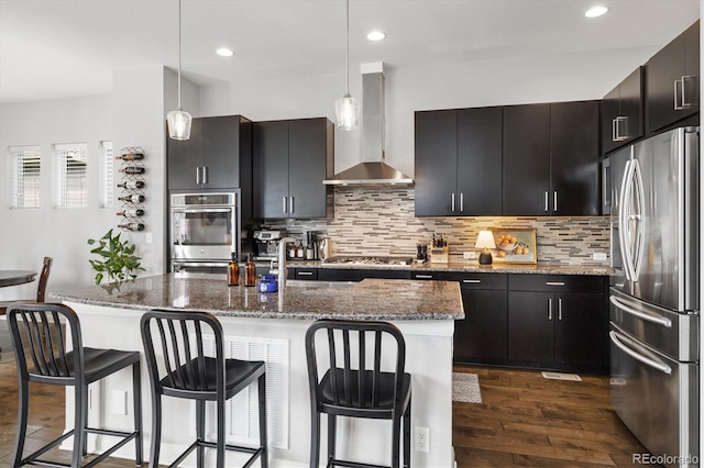 kitchen with stainless steel appliances, dark wood finished floors, decorative backsplash, hanging light fixtures, and wall chimney range hood