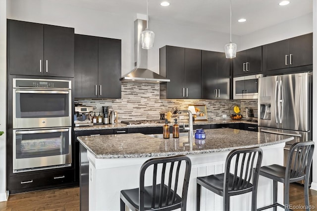 kitchen with decorative backsplash, wall chimney exhaust hood, stainless steel appliances, and dark cabinets
