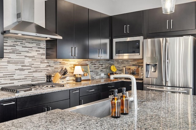 kitchen featuring wall chimney range hood, dark cabinets, and appliances with stainless steel finishes