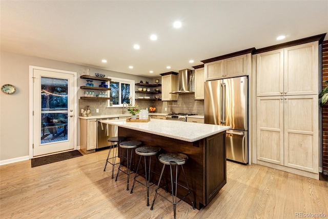 kitchen with wall chimney range hood, a kitchen bar, open shelves, light wood-style floors, and stainless steel appliances