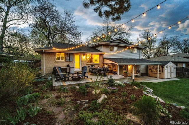 rear view of house featuring a storage shed, a deck, brick siding, an outdoor structure, and an outdoor fire pit