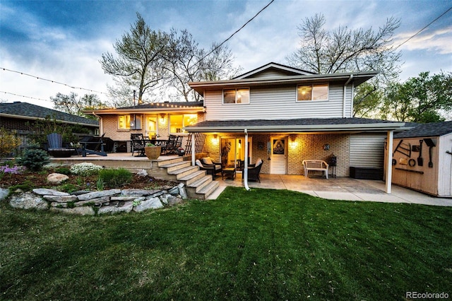 back of house with a lawn, a patio, an outbuilding, and brick siding