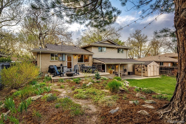 back of house featuring an outdoor structure, a fire pit, a patio, a storage unit, and a lawn