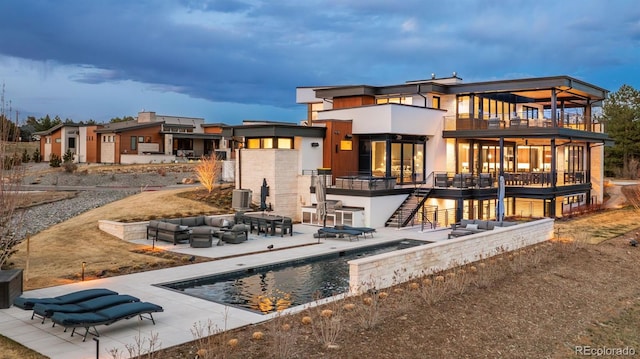 rear view of property with stairs, a patio area, outdoor lounge area, a balcony, and an outdoor pool