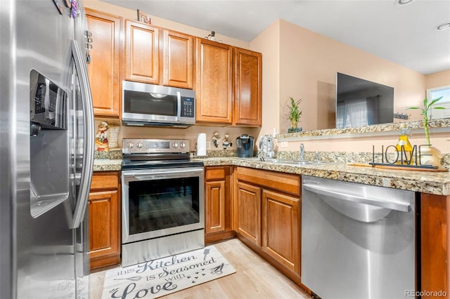 kitchen featuring sink, appliances with stainless steel finishes, light hardwood / wood-style floors, light stone countertops, and kitchen peninsula