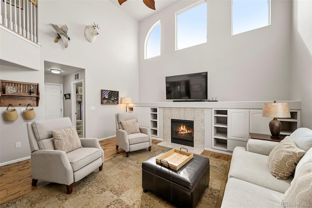 living room with visible vents, baseboards, a tiled fireplace, ceiling fan, and light wood-type flooring