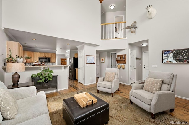 living room featuring light wood-type flooring, a towering ceiling, and baseboards