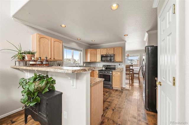 kitchen with light countertops, light brown cabinetry, appliances with stainless steel finishes, a peninsula, and a kitchen bar