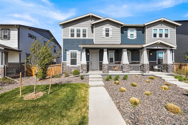 craftsman-style house with covered porch, stone siding, a front yard, and fence