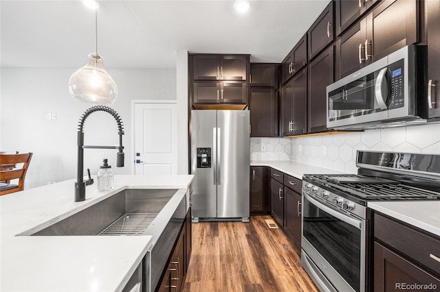 kitchen with appliances with stainless steel finishes, light countertops, a sink, and wood finished floors