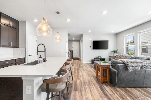 kitchen with a breakfast bar, recessed lighting, decorative backsplash, a sink, and light wood-type flooring