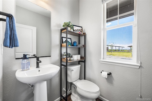 bathroom featuring baseboards, a textured wall, and toilet