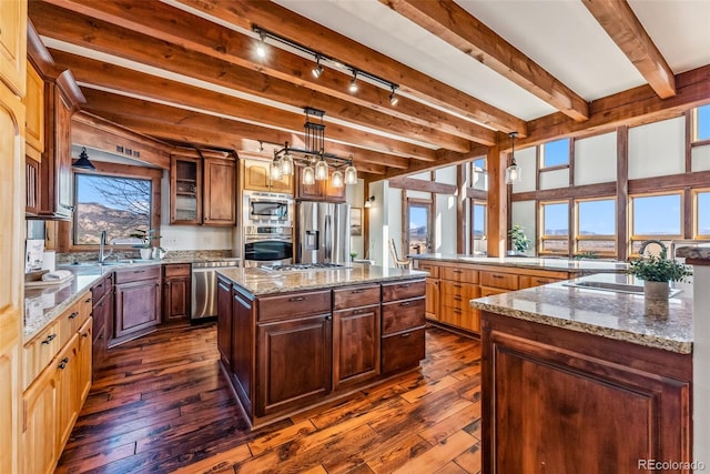 kitchen with stainless steel appliances, dark wood finished floors, light stone counters, track lighting, and a kitchen island