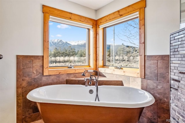 full bath with tile walls, a freestanding tub, and a mountain view