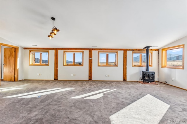 unfurnished living room with baseboards, lofted ceiling, a wood stove, and carpet