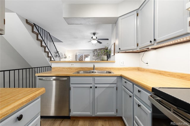 kitchen with ceiling fan, a peninsula, stainless steel dishwasher, light wood-style floors, and a sink