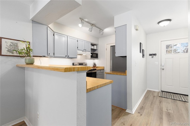 kitchen with a peninsula, light wood-style floors, butcher block countertops, and stainless steel appliances