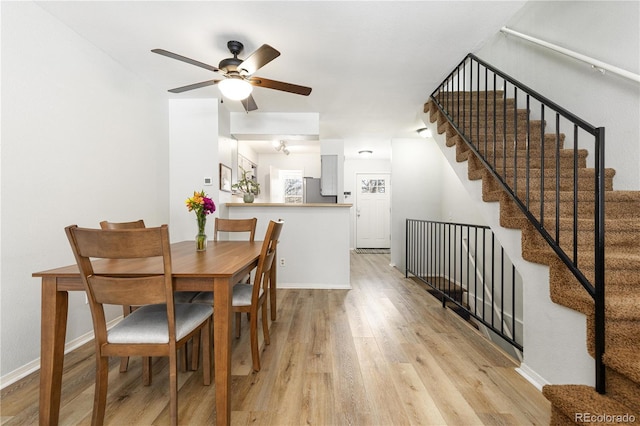 dining room with light wood finished floors, stairway, a ceiling fan, and baseboards