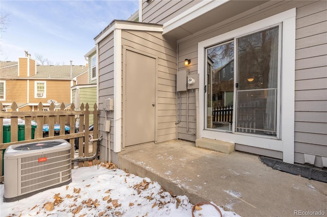 snow covered property entrance with central AC unit and fence