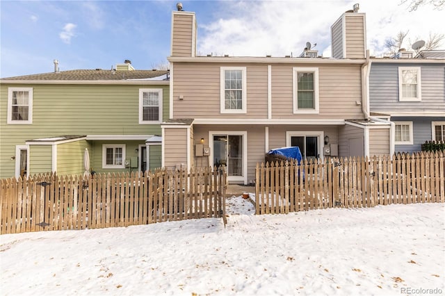 snow covered house with a fenced front yard and a chimney