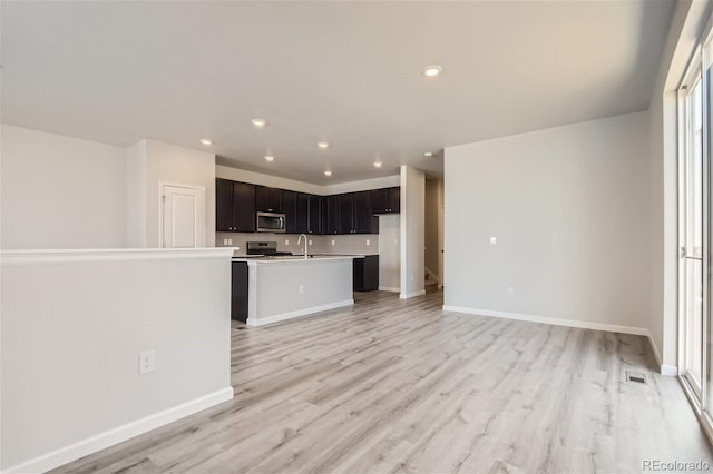 kitchen with appliances with stainless steel finishes, an island with sink, sink, backsplash, and light hardwood / wood-style flooring