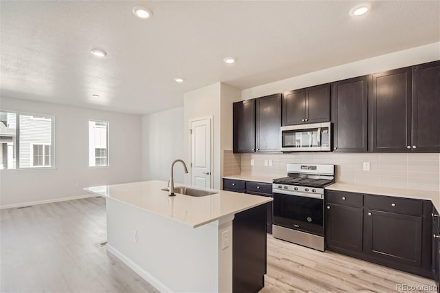 kitchen with sink, an island with sink, stainless steel appliances, light hardwood / wood-style floors, and decorative backsplash