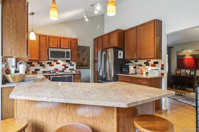 kitchen featuring pendant lighting, appliances with stainless steel finishes, light hardwood / wood-style floors, kitchen peninsula, and a breakfast bar area