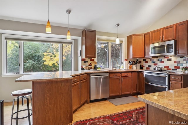 kitchen with a kitchen bar, stainless steel appliances, sink, decorative light fixtures, and light hardwood / wood-style floors